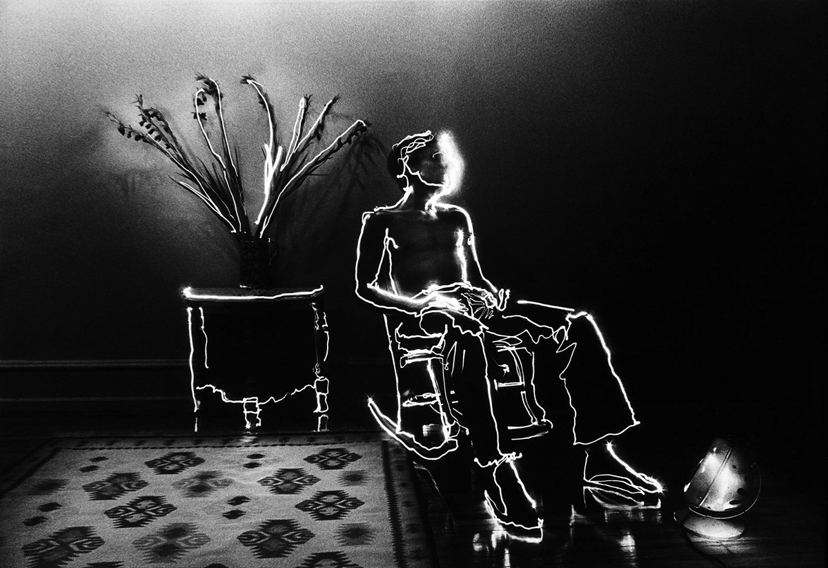 A black and white photograph by David Lebe depicting a person sitting in a chair outlined by rays of light. The work is called Barry In Rocker.